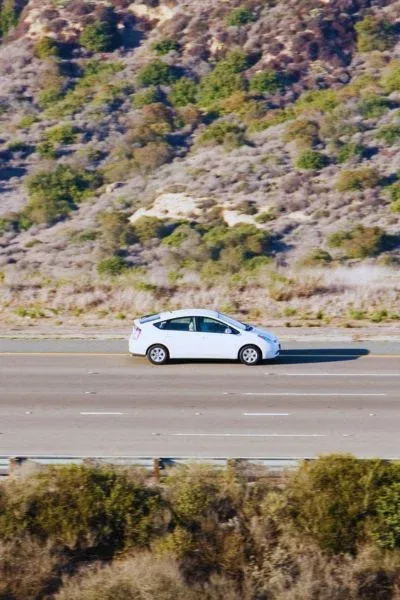 Voiture hybride blanche roulant sur une route à flanc de colline